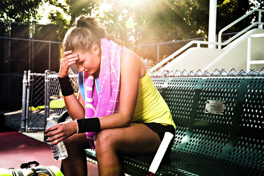 Female tennis player on bench with head in hands
