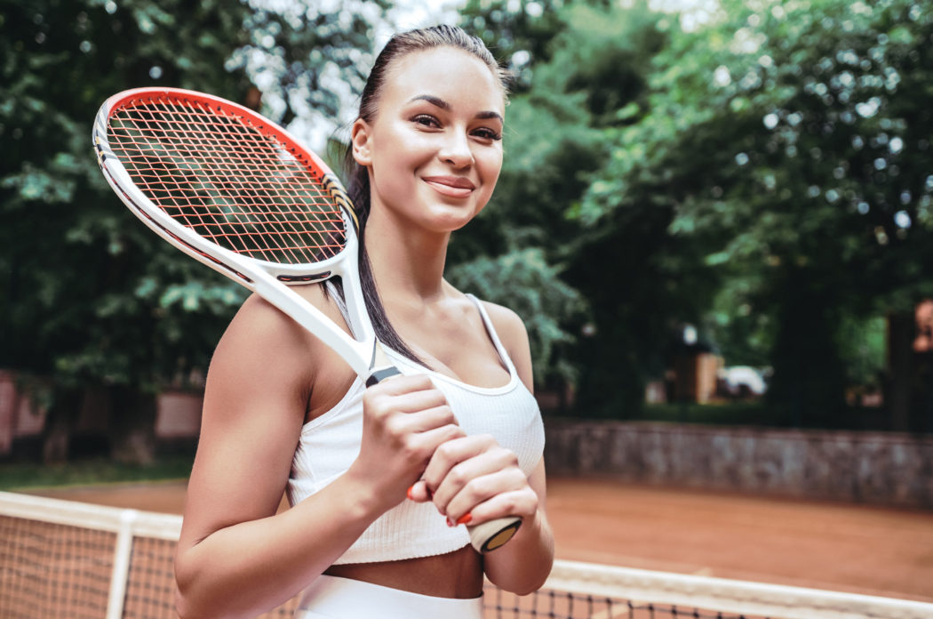 Feeling confident of winning. Beautiful young woman holding tennis racket and looking happy