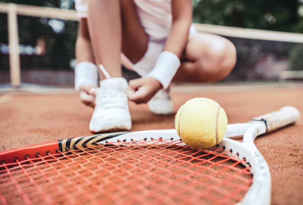 Girl on tennis court in the sport club. Cropped image of a little tennis player. Girl child tying shoelaces on tennis court. Summer activities for children.