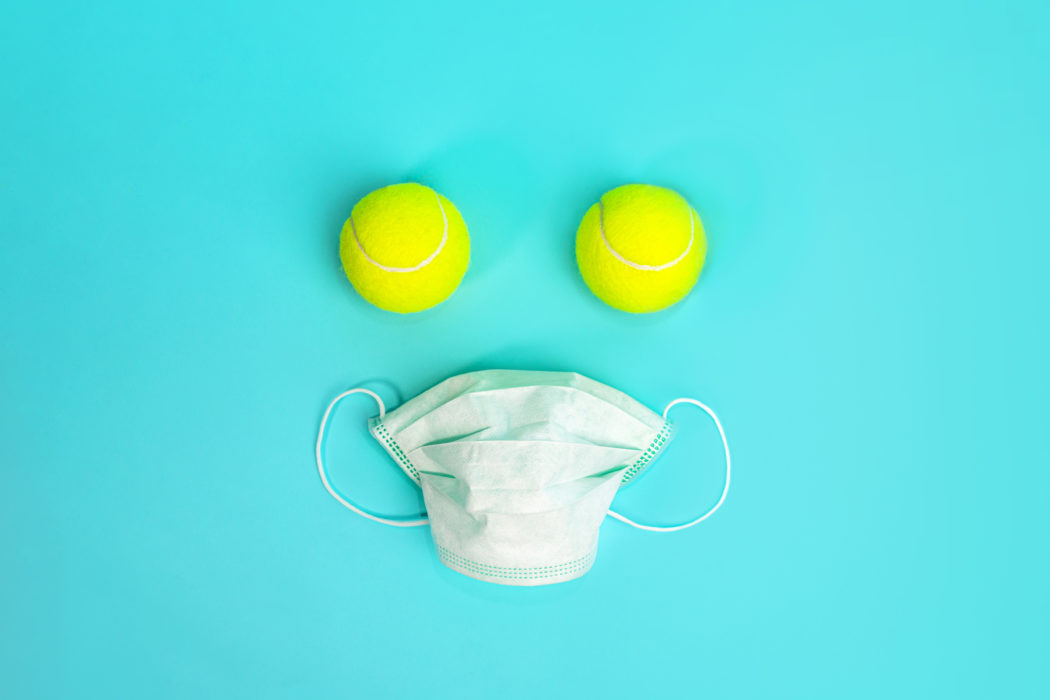 Pandemic idea with tennis balls and medical surgical mask on blue green mint background.