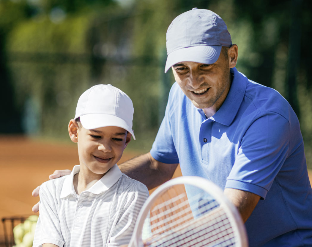 Tennis Lesson. Smiling Coach Explaining Tennis Technique to a Boy